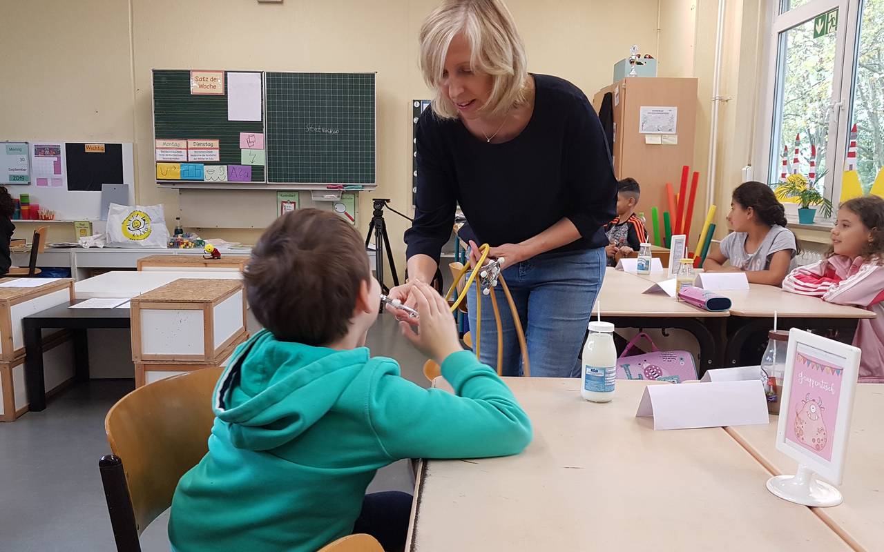 Gesundheitsförderin Heike Eckey zeigt, wie die Kinder mit einem Stethoskop den Herzschlag hört.