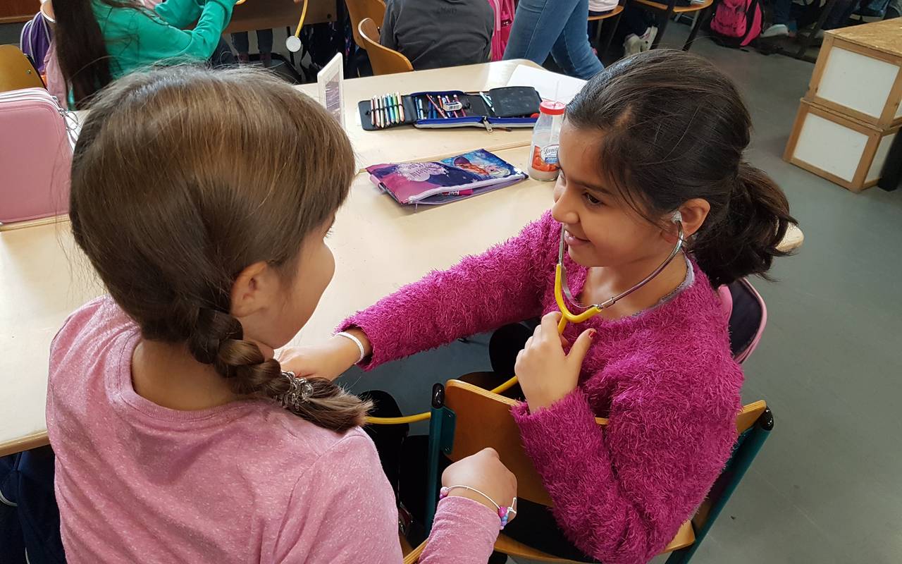 Zwei Mädchen nehmen am Unterricht "Klasse2000" teil und hören ihren Herzschlag an.