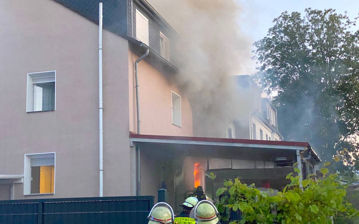 Zwei Feuerwehrmänner stehen vor einem brennenden und qualmenden Haus
