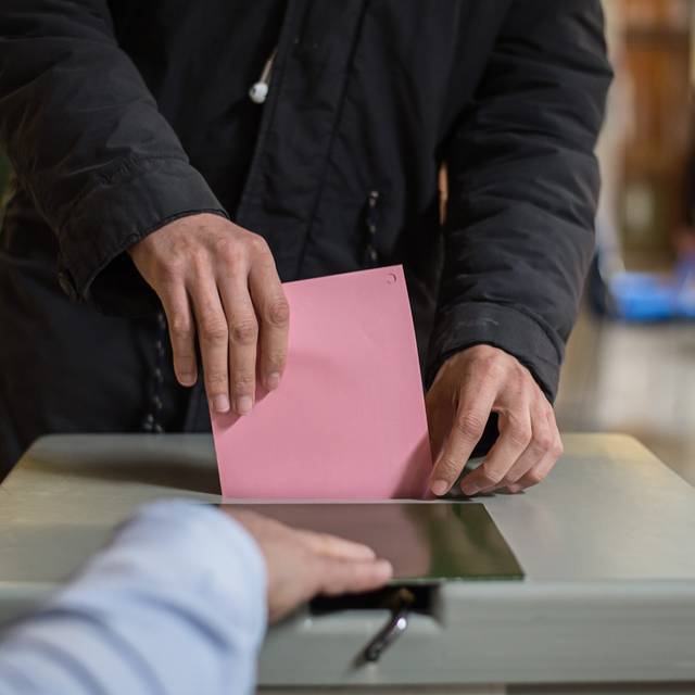 Ein Wahlzettel wird in eine Wahlurne gesteckt.