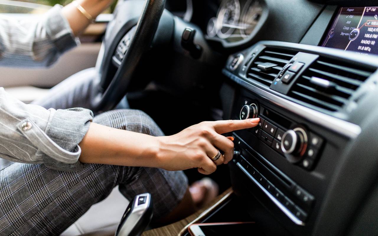 Frau sitzt im Auto und schaltet Radio ein.