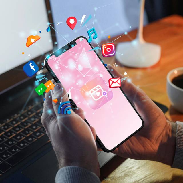 Jemand hält ein Handy in der Hand. Um das Handy herum sind Symbole von sozialen Medien und anderen Symbolen vom Handy