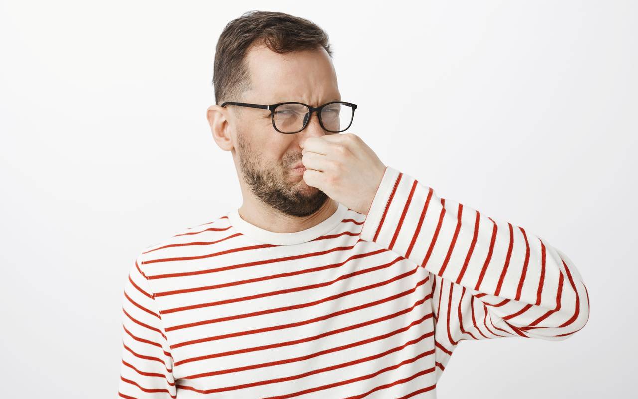 Mann der sein Gesicht verzieht und sich die Nase zu hält.