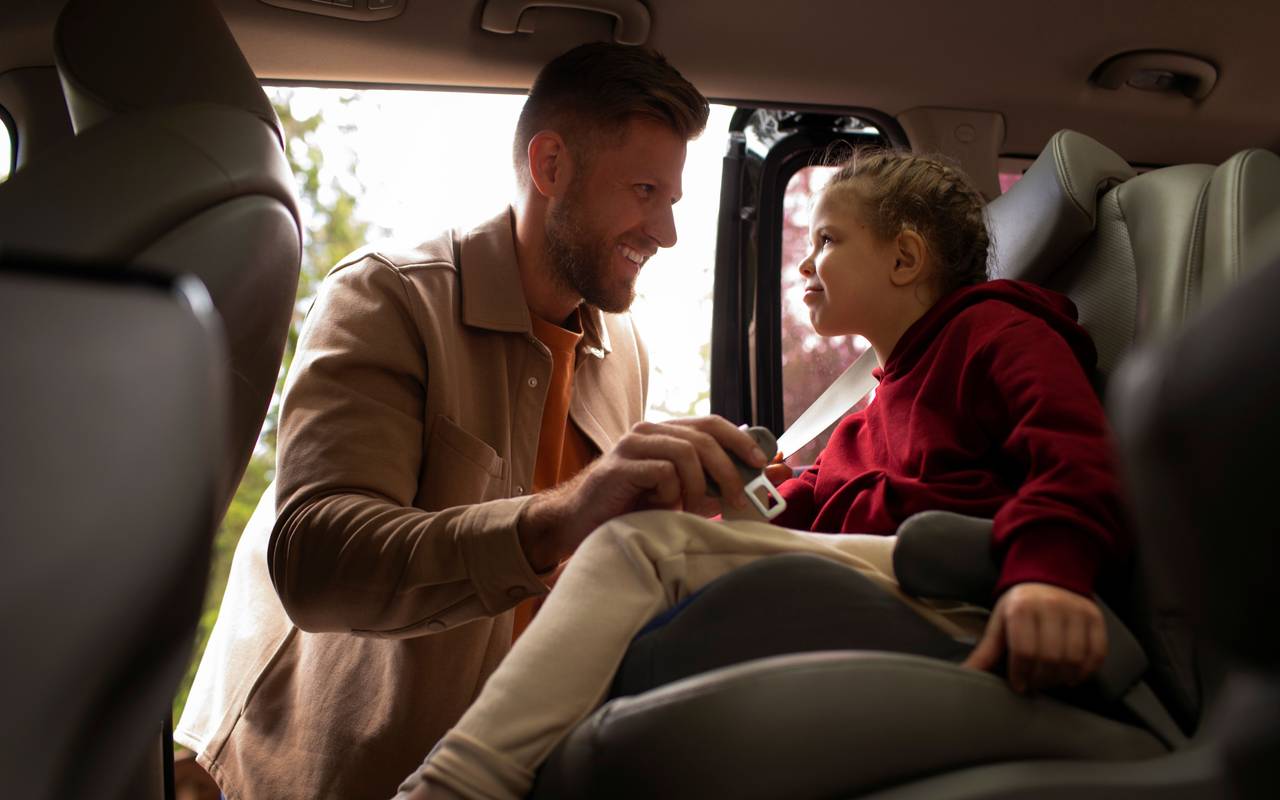 Vater schnallt Tochter im Auto im Kindersitz an