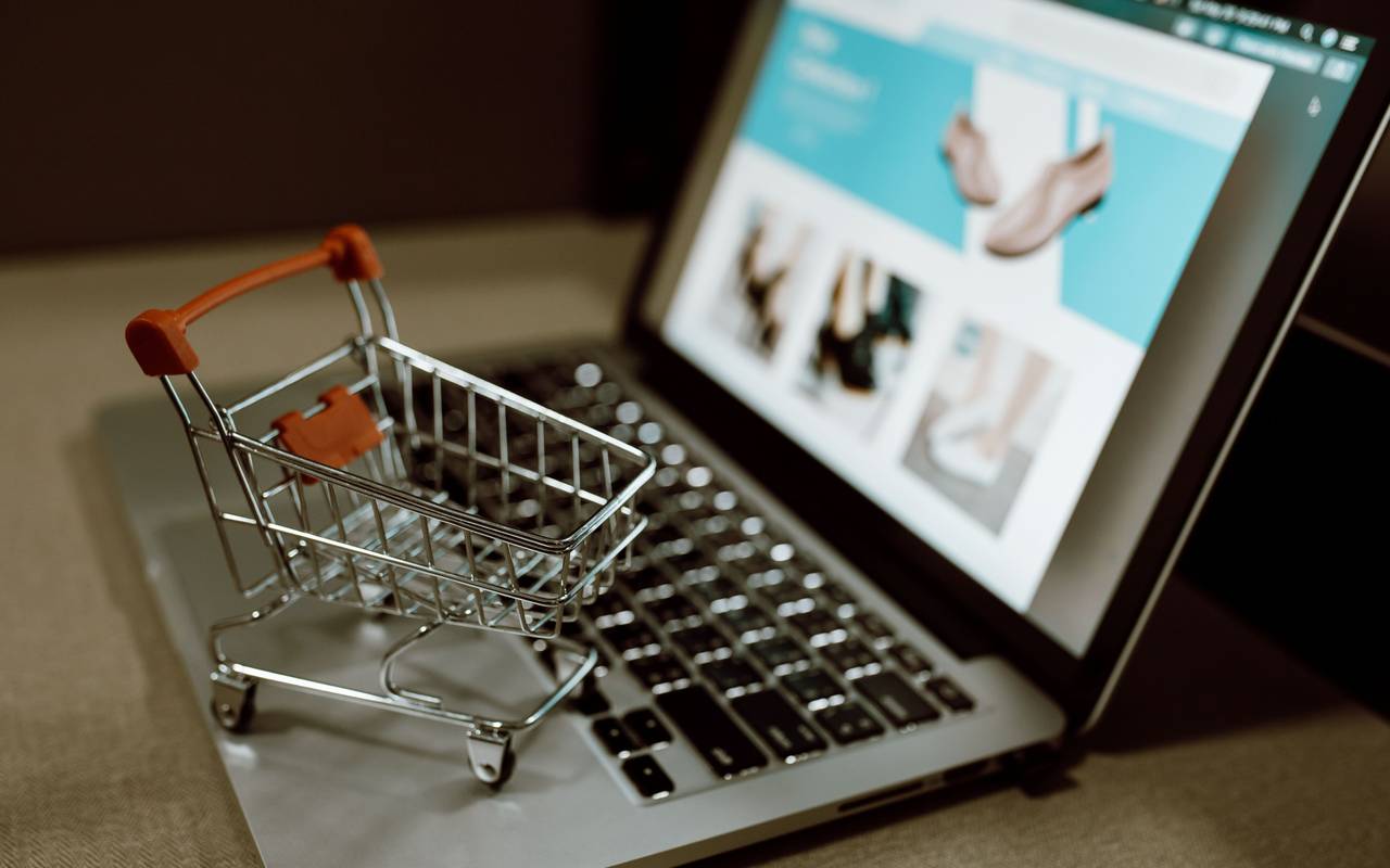 Aufgeklappter Laptop auf dem ein Miniatur Einkaufswagen steht