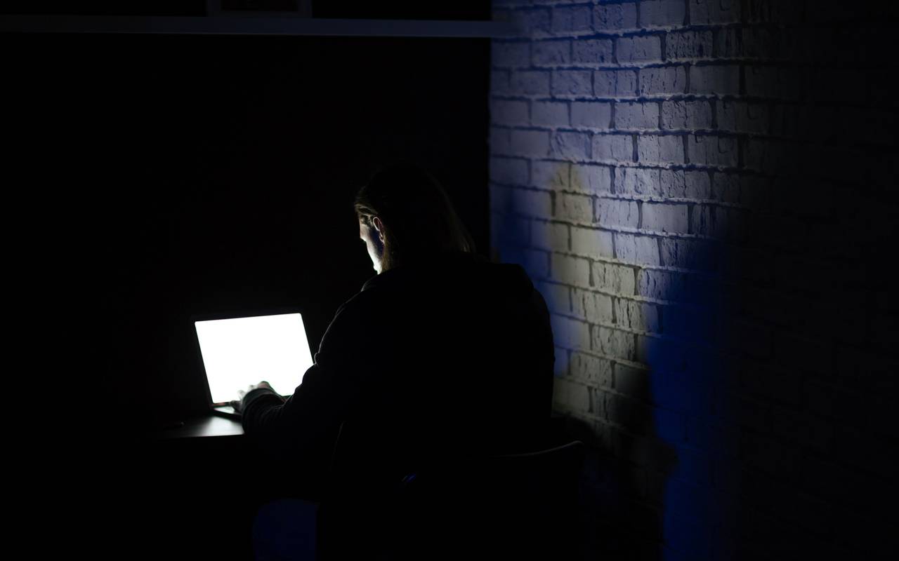 Ein Mann sitzt im dunkeln an einem Laptop