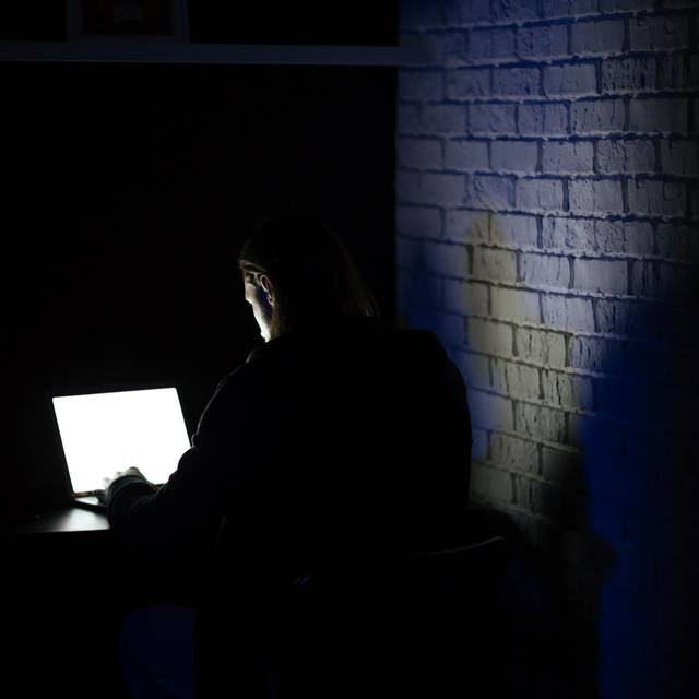 Ein Mann sitzt im dunkeln an einem Laptop
