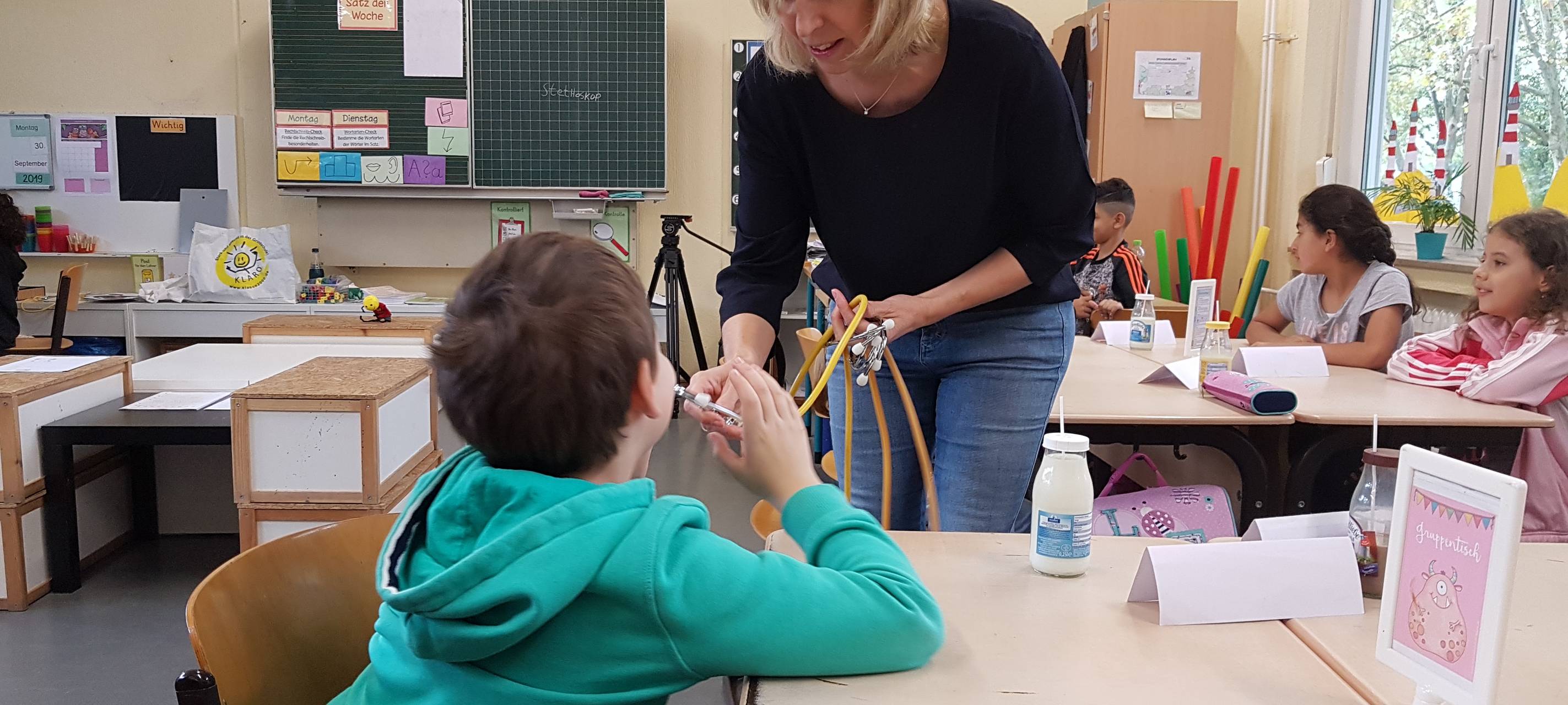 Gesundheitsförderin Heike Eckey  zeigt, wie die Kinder mit einem Stethoskop den Herzschlag hört.