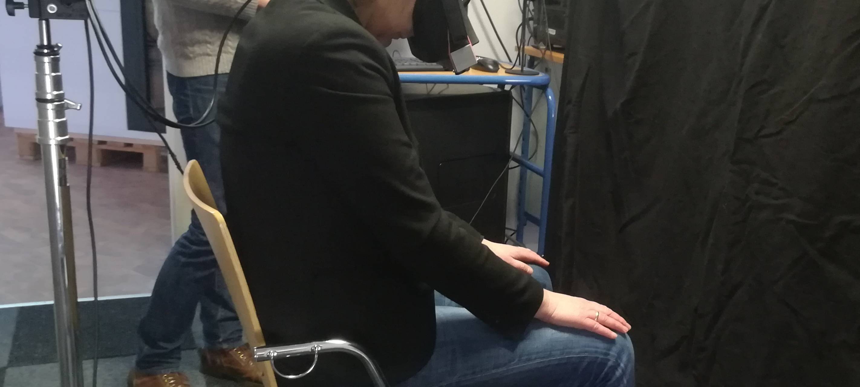 Junge Frau sitzt mit gesenktem Kopf und trägt eine dunkle VR-Brille.