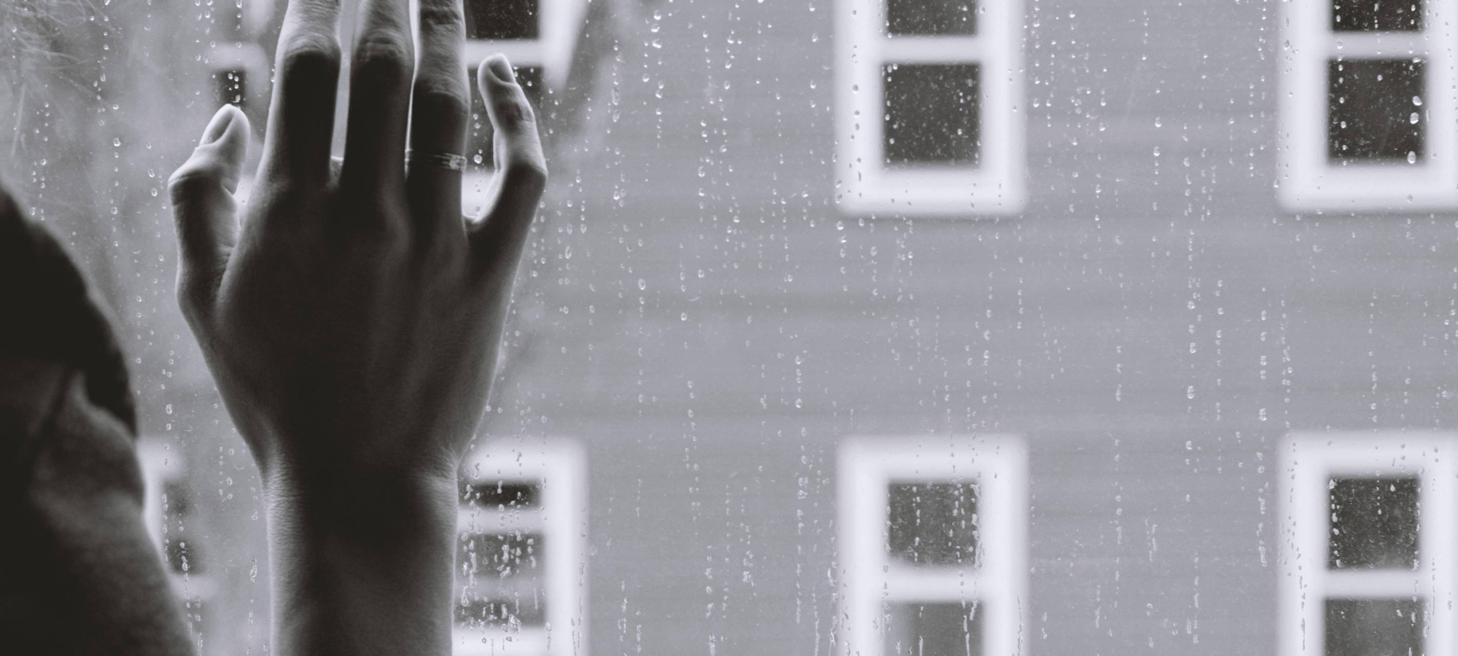 Frau steht am Fenster. Symbolbild.