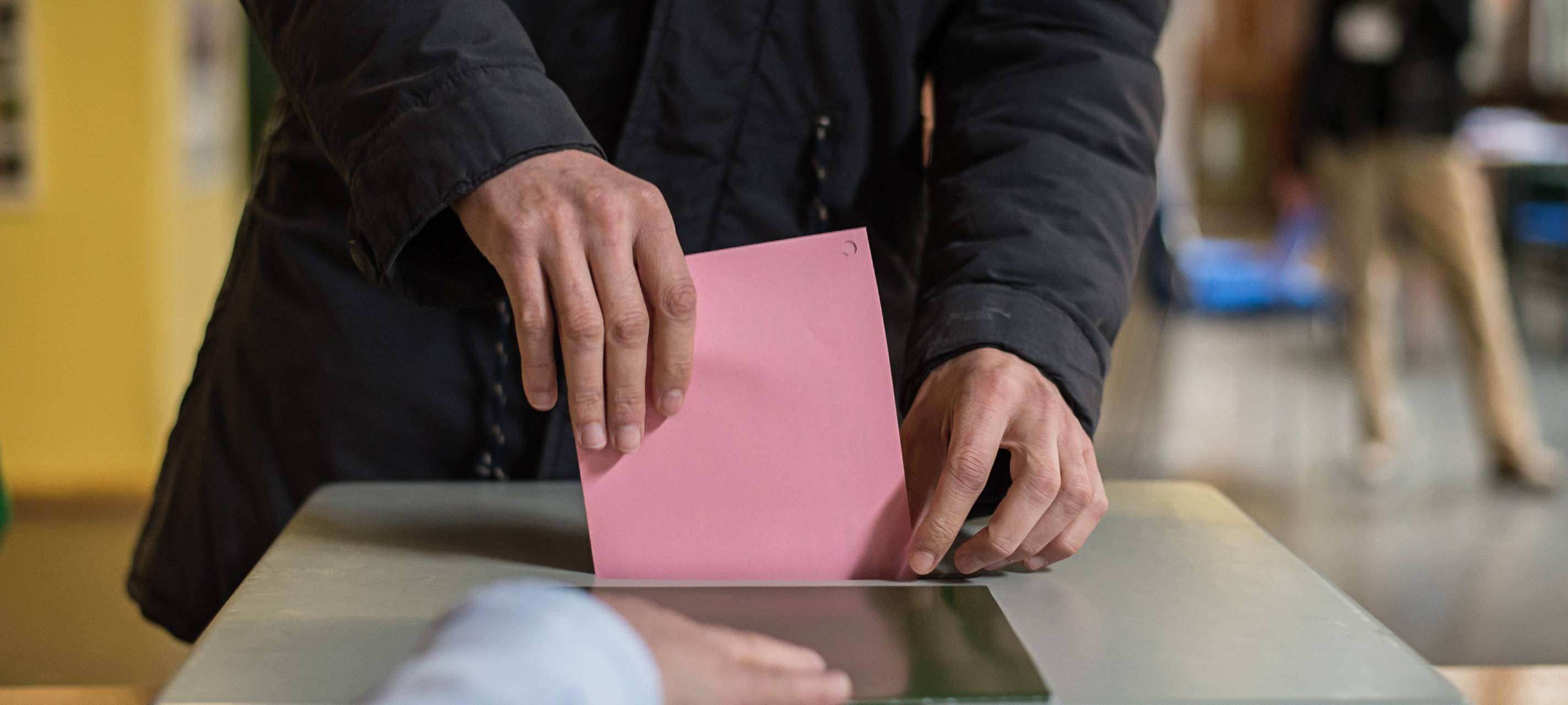 Ein Wahlzettel wird in eine Wahlurne gesteckt.