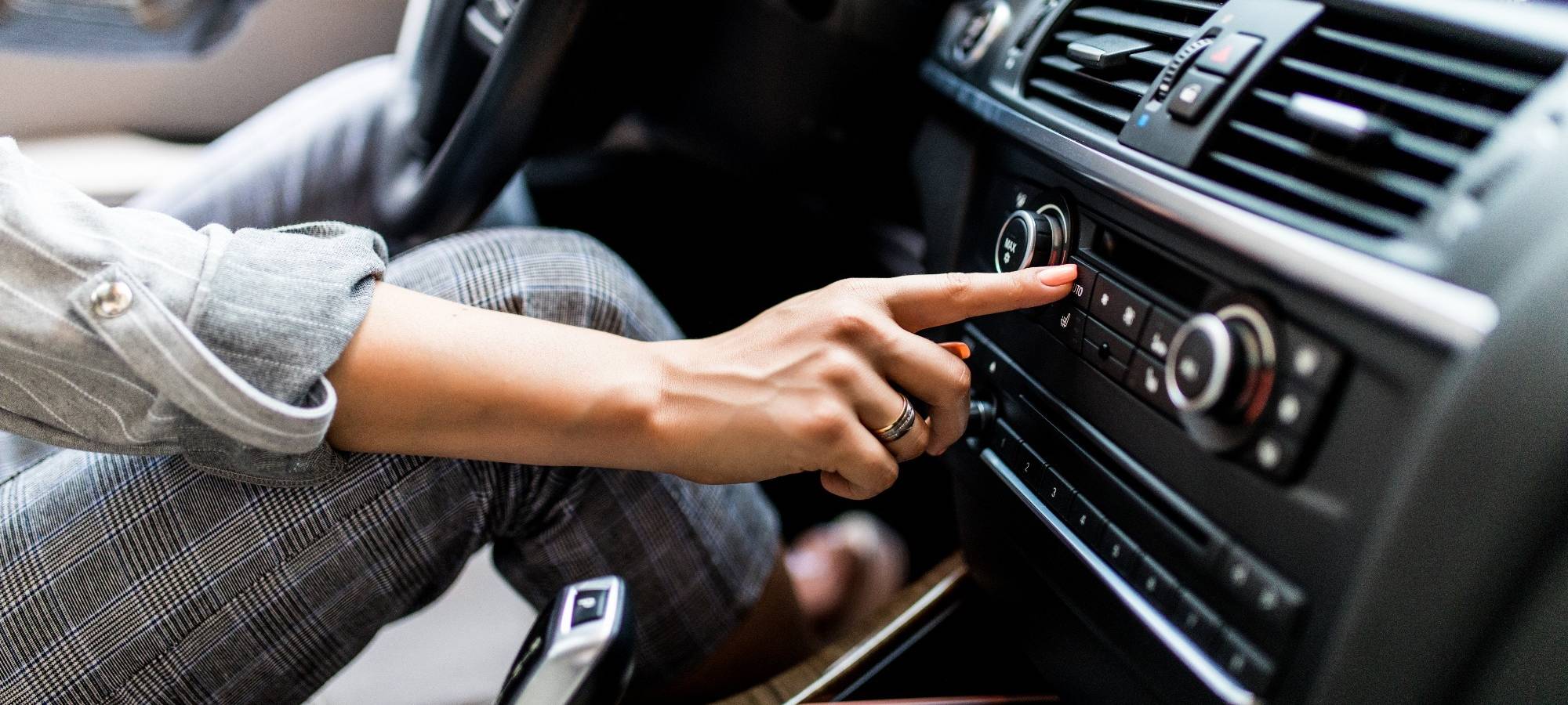 Frau sitzt im Auto und schaltet Radio ein.