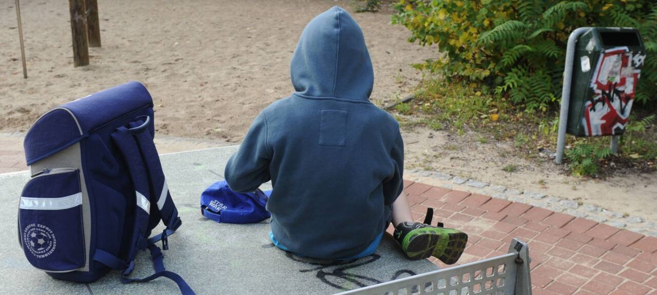 Ein Junge sitzt mit seinem Schulranzen auf einer Tischtennisplatte auf einem Spielplatz. Notorische Schwänzer oder Eltern, die ihre Kinder für einen frühzeitigen Urlaubsbeginn krank schreiben: Eine Verletzung der Schulpflicht kann unangenehme Folgen haben.
