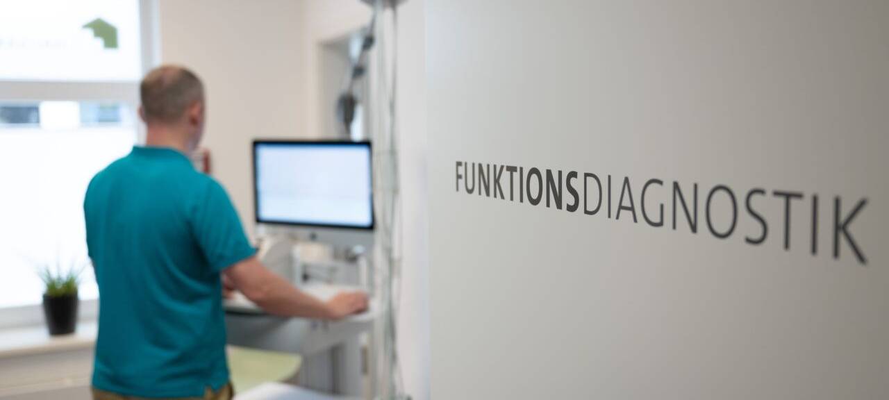 Ein Arzt führt in ein Behandlungszimmer ein funktionelles Gerät. Auf einer Schrift steht Funkionsdiagnostik.