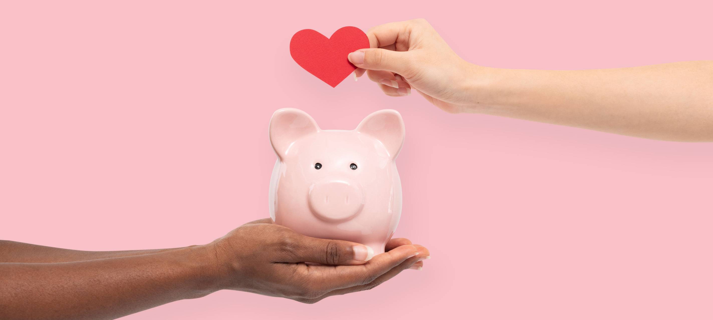 Eine Person hält ein Sparschwein in der Hand und die andere hält ein rotes herz darüber