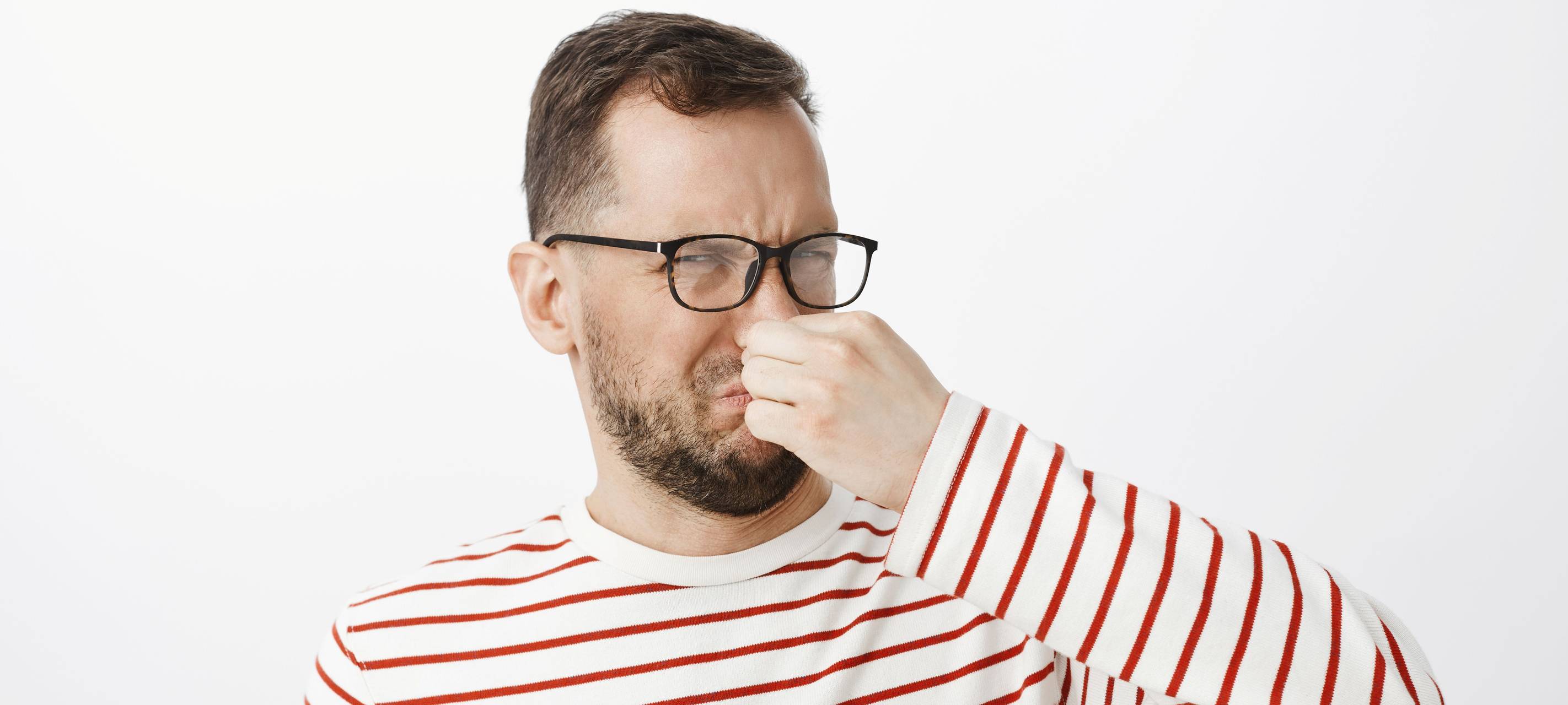 Mann der sein Gesicht verzieht und sich die Nase zu hält.