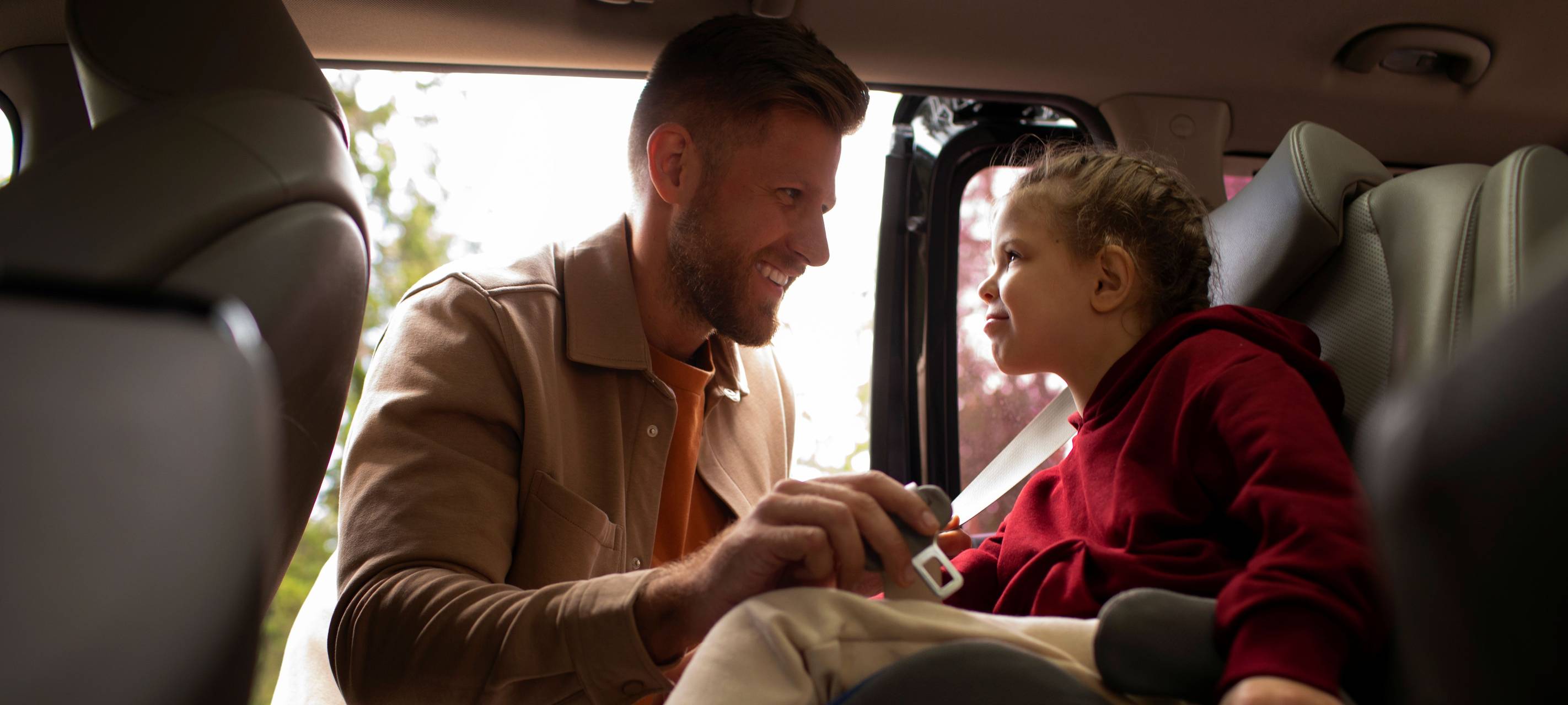 Vater schnallt Tochter im Auto im Kindersitz an
