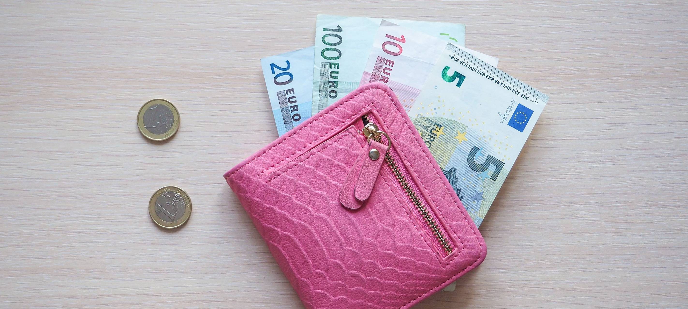 Rosa Portmonee mit Geldscheinen drin. Neben dem Portmonee liegen Münzen