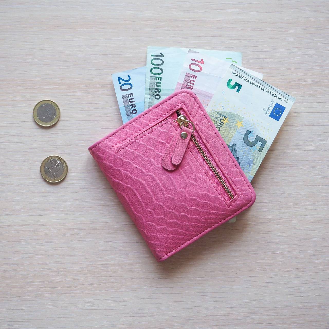 Rosa Portmonee mit Geldscheinen drin. Neben dem Portmonee liegen Münzen