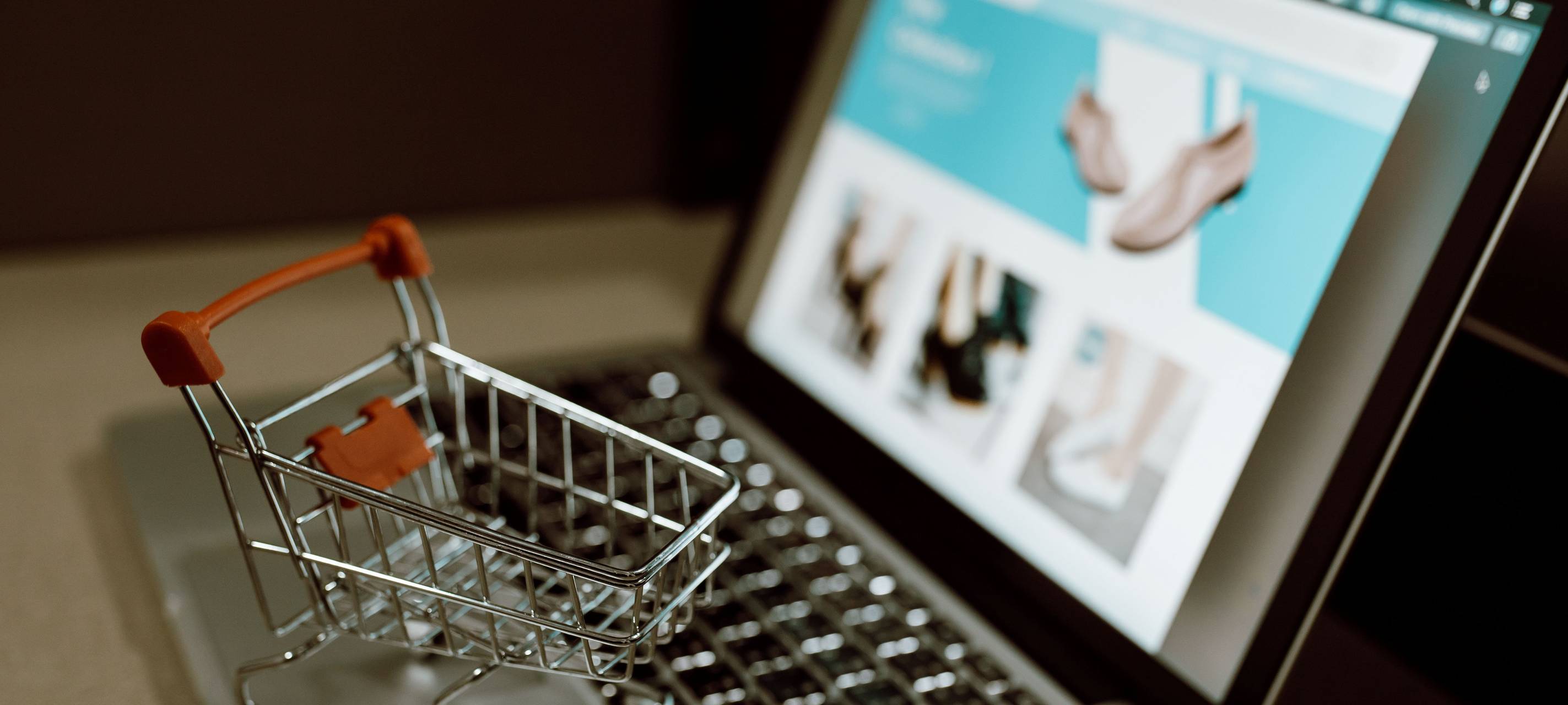 Aufgeklappter Laptop auf dem ein Miniatur Einkaufswagen steht