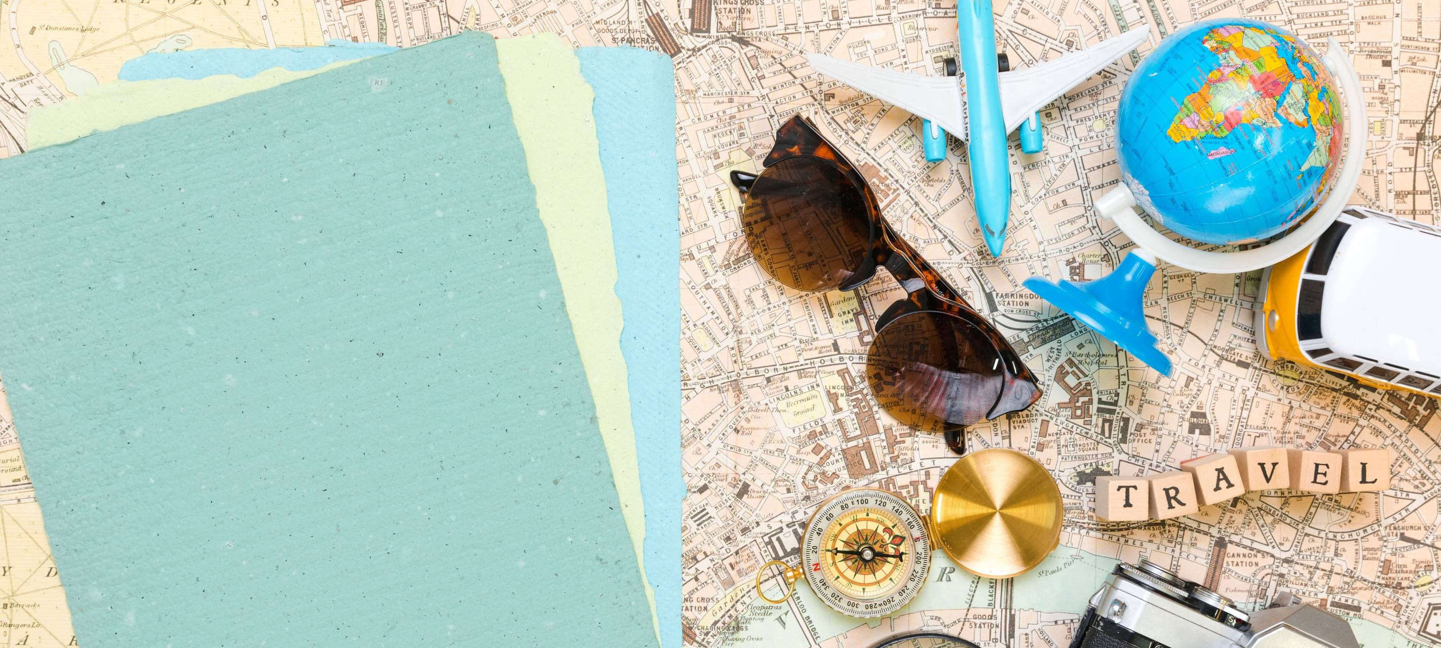 Auf einem Tisch liegen eine Karte, ein Flugzeug, Steine auf denen "Travel" steht und ein Globus