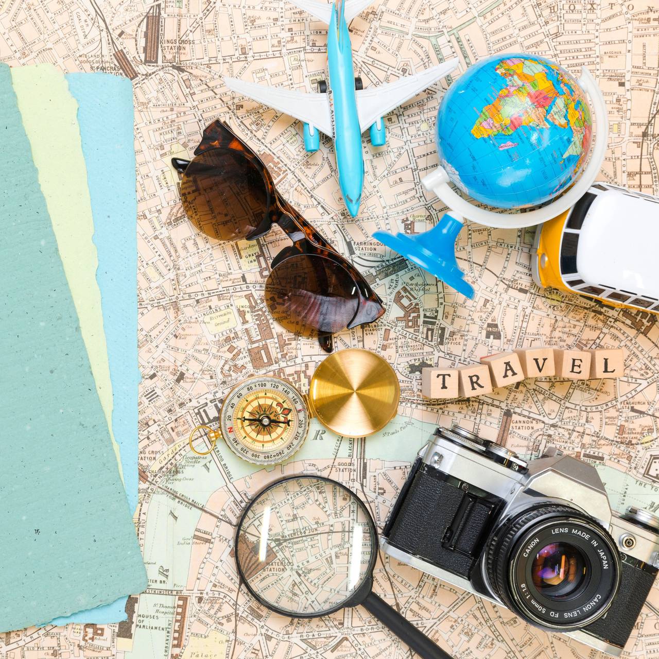 Auf einem Tisch liegen eine Karte, ein Flugzeug, Steine auf denen "Travel" steht und ein Globus