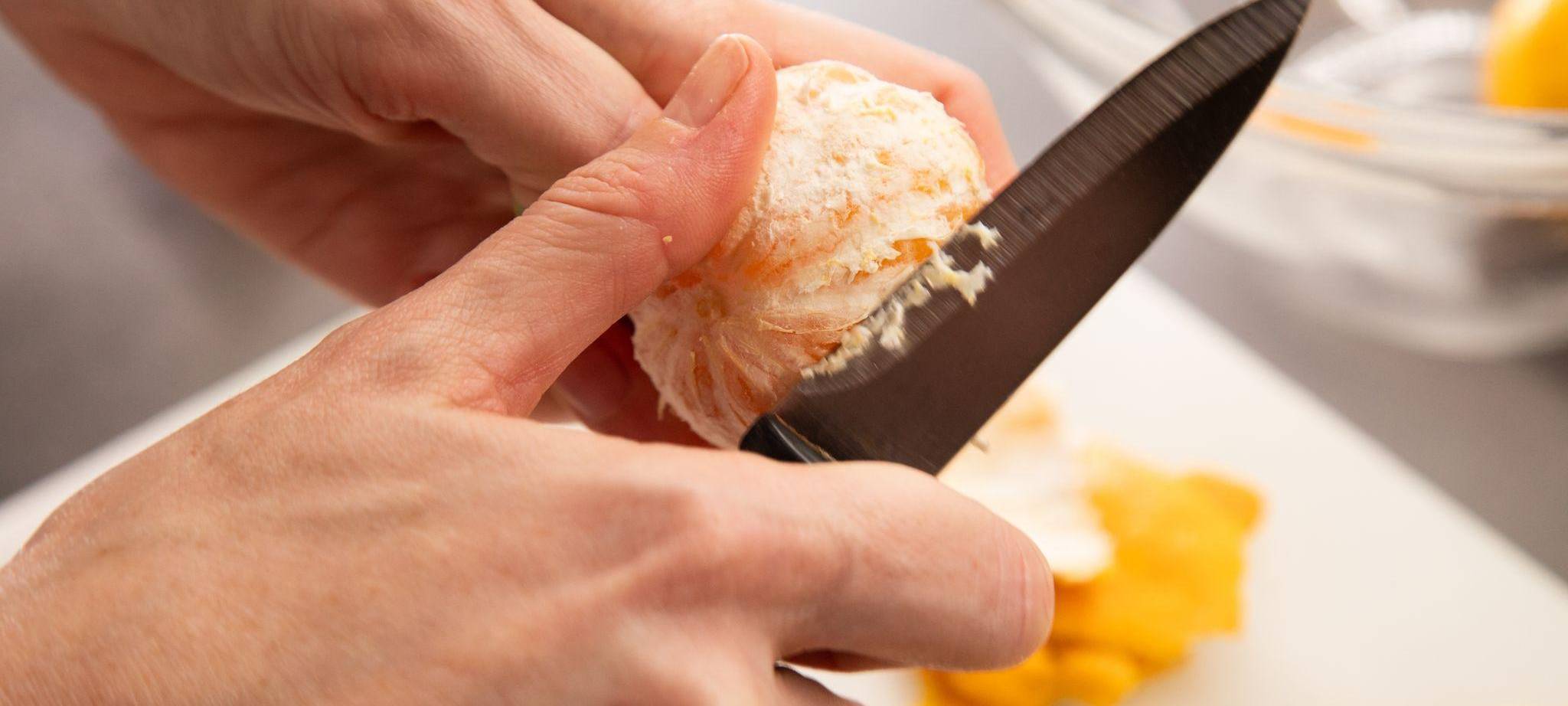 Eine Clementine wird mit einem Messer geschält