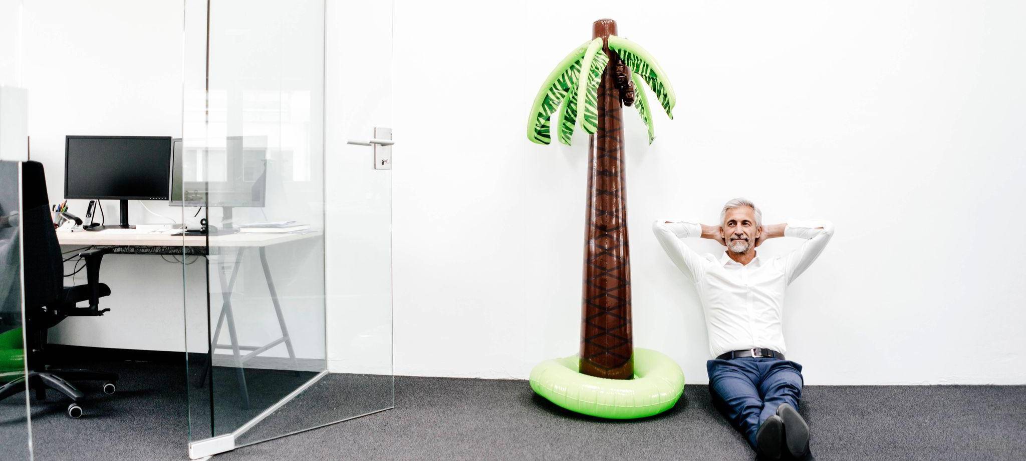 Mann sitzt im Büro neben einer aufblasbaren Palme