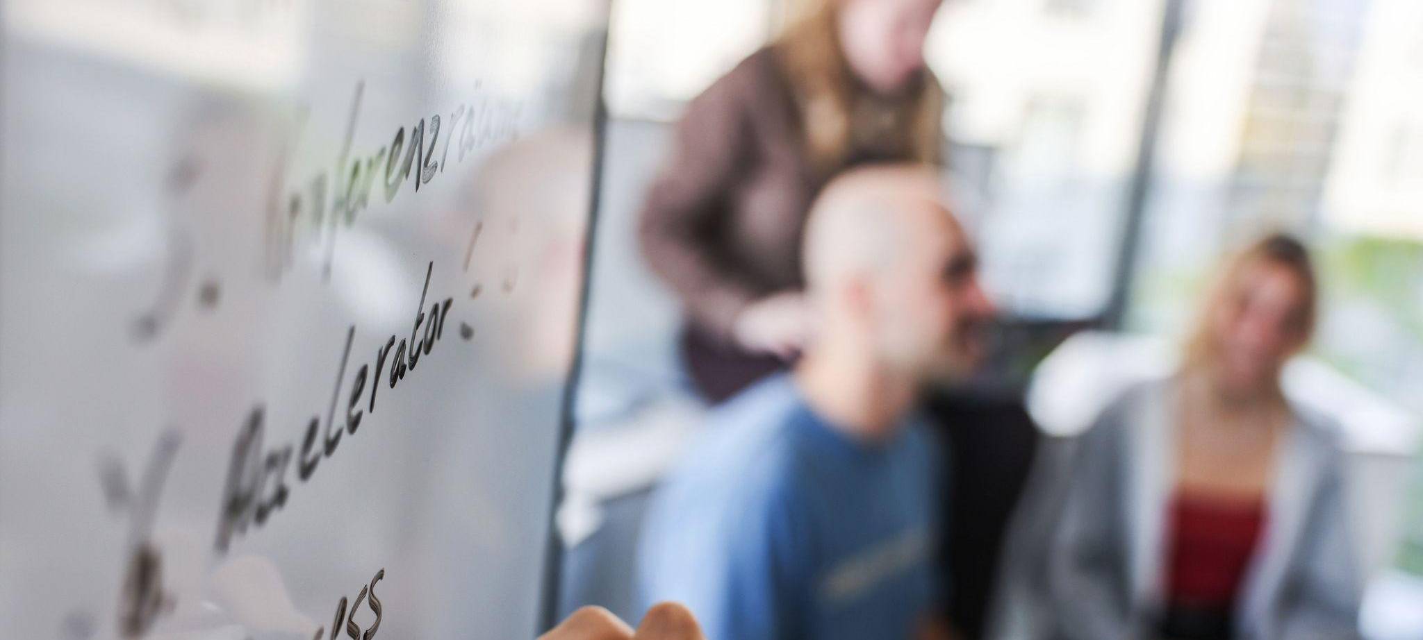 Eine Person schreibt mit schwarzem Marker auf ein Whiteboard