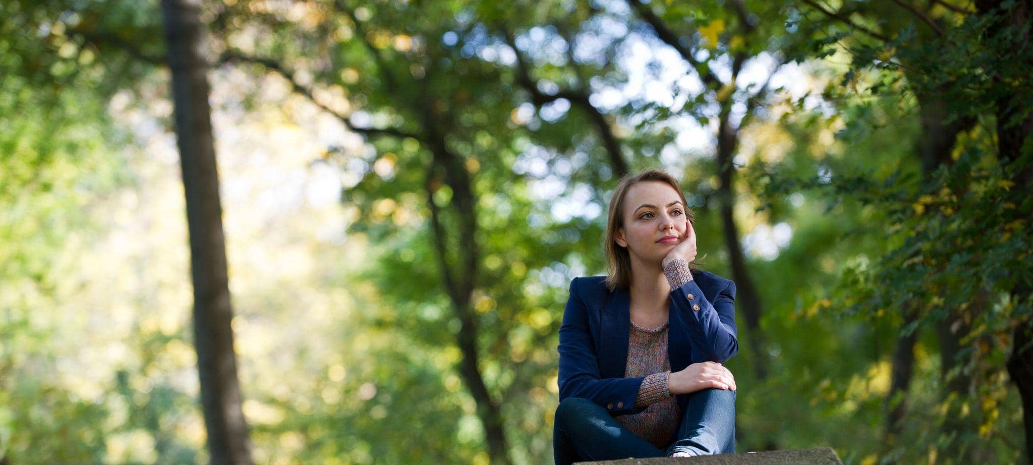 Eine Frau sitzt nachdenklich auf einer Mauer im Park